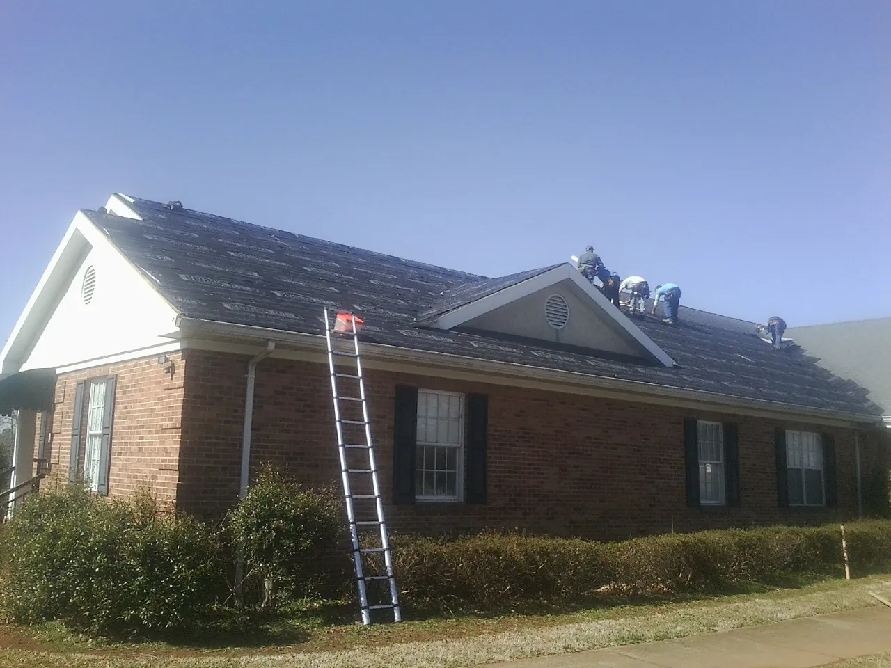 Crew tearing shingles off a brick ranch roof with a ladder set — Emergency Roof Repair work by our crew in Soda Springs